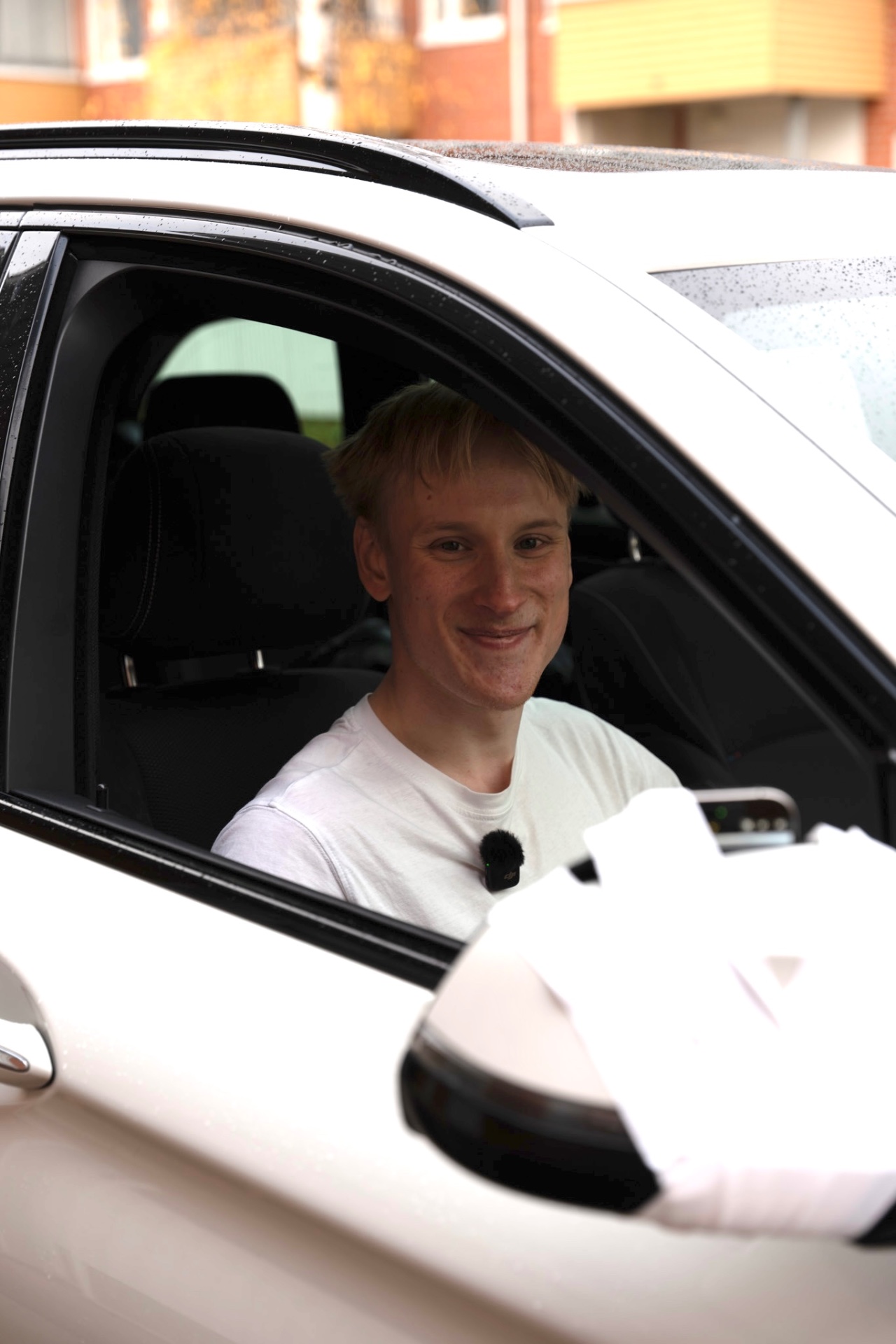 Jani Aleksi hymyilee autossa mikrofoni rinnassa